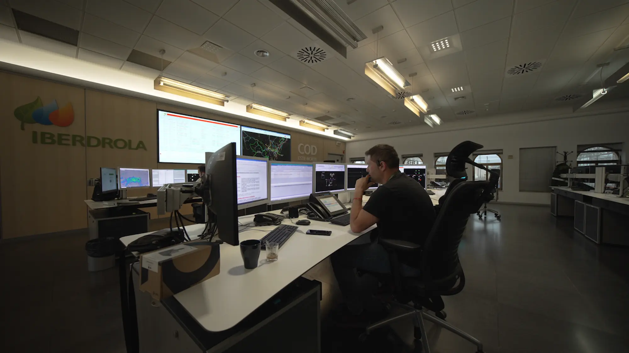 Un operador sentado en una sala de control, trabajando frente a varias pantallas y monitores.